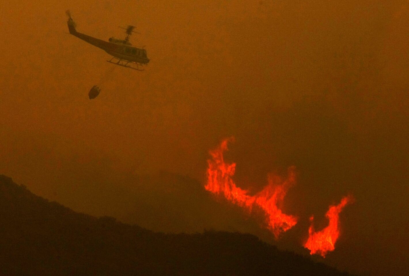 A helicopter prepares to drop a load of water on the Powerhouse fire that burned hundreds of acres in the Green Valley area Thursday.
