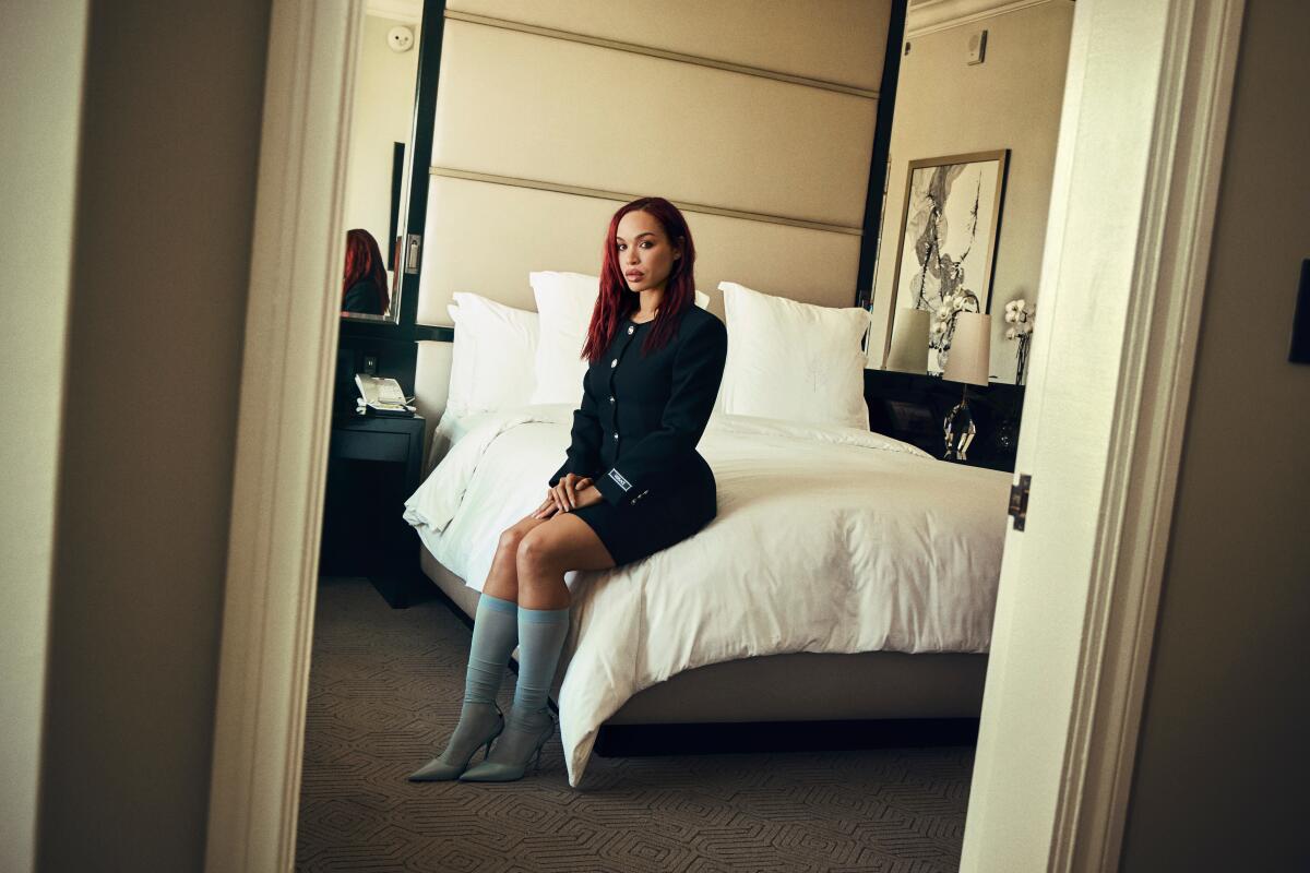 A woman sits on a bed in a hotel suite.
