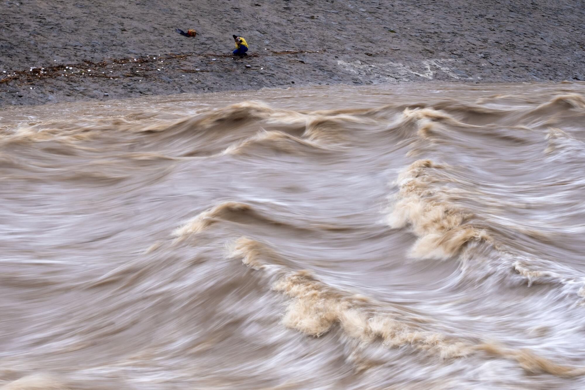 A person takes photos of a turbulent river.
