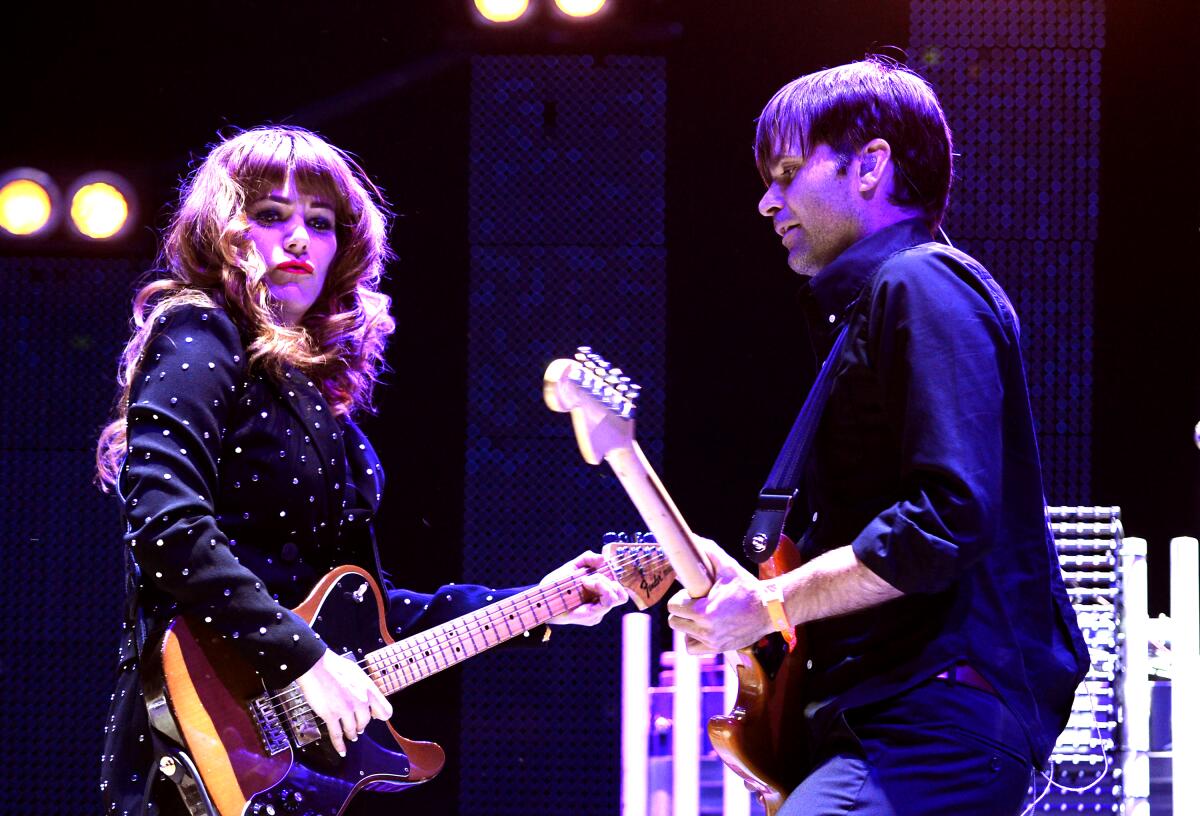 Jenny Lewis, in a bedazzled suit, and Ben Gibbard play guitar on stage.