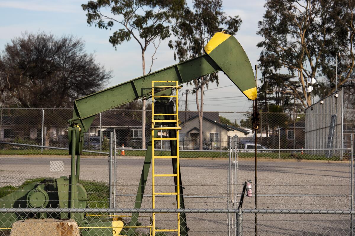 Homes are seen behind a green and yellow pumpjack inside the Wilmington Athletic Complex in Los Angeles.