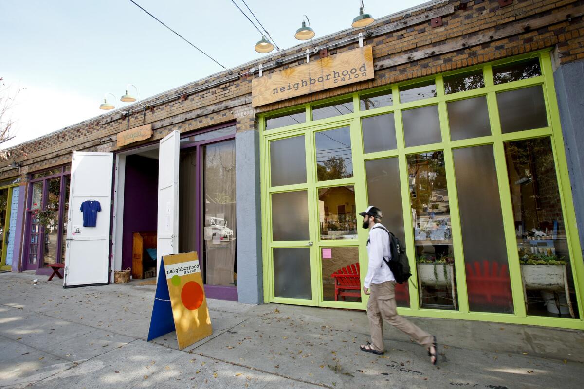 A pedestrian walks by a colorful series of stores, including the Neighborhood Salon and Yogala, along Echo Park Avenue.