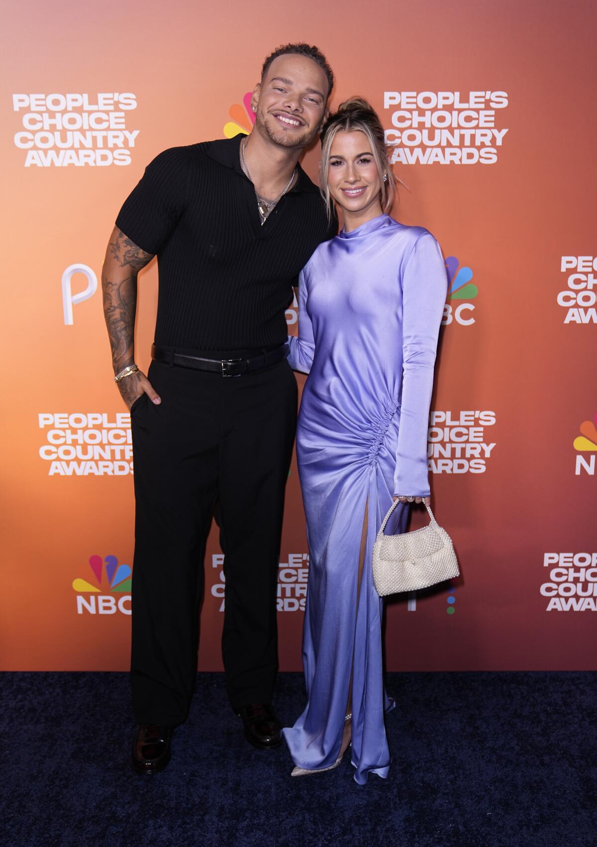 Kane Brown wears a black shirt and pants and Katelyn Brown wears a long-sleeved lavender gown as they pose for photos 