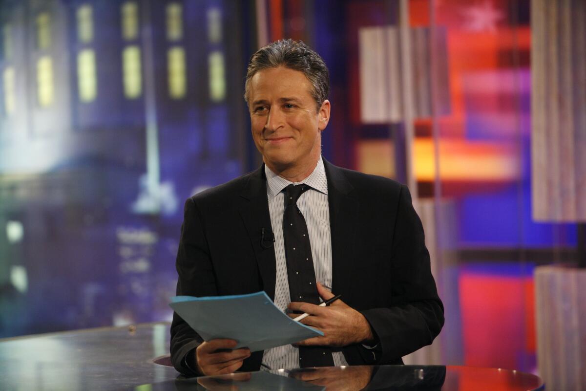 A man in a suit and tie on the set of "The Daily Show" in 2006, holding paper and a pen