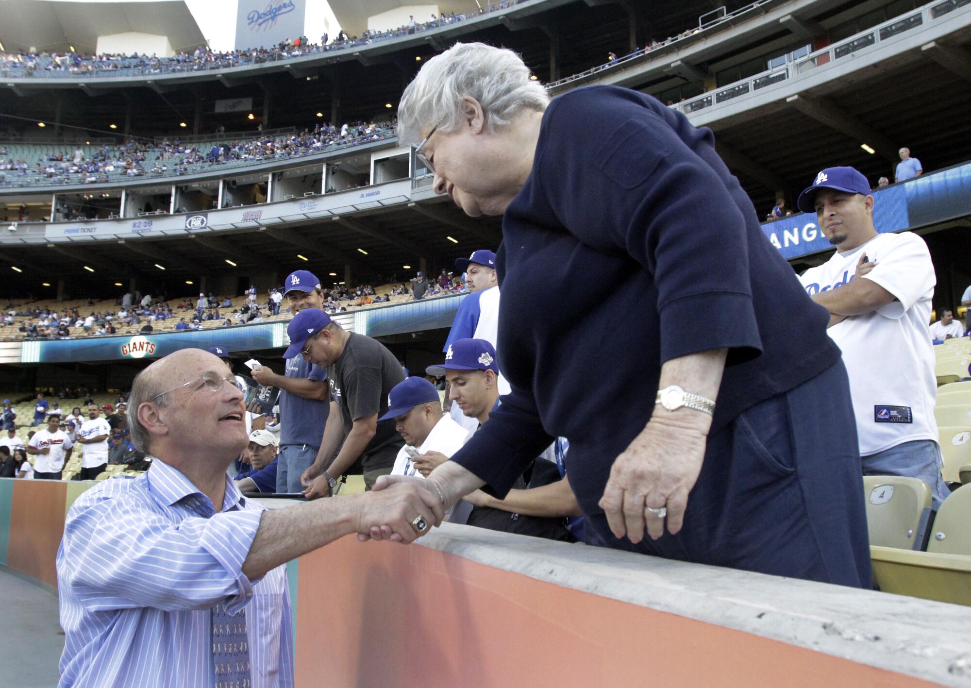 A man shakes hands with a woman across a barrier separating the stadium stands from the baseball field.