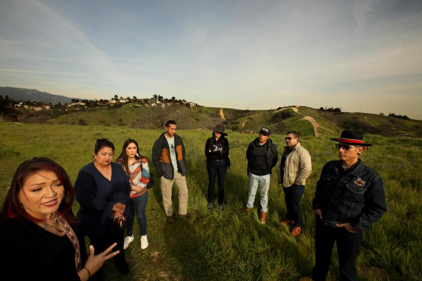 LOS ANGELES, CA - FEBRUARY 16, 2023 - Gabrielino Shoshone Tribe members Jaime Rocha, from left, her mother Eileen Rocha, Jaime's sister Cheyenne Rocha, along with Tecpatl Kuauhtzin, Minnie Ferguson, Victorino Torres-Nova, Trinidad Ruiz and Marcos Aguilar, right, all from the Anahuacalmecac International University Preparatory of North America, stand on a vacant site where an extension of their school will be built in El Sereno on February 16, 2023. In Sept. 2022, the Anahuacalmecac International University Preparatory of North America, a K-12 Indigenous charter school based in El Sereno, purchased 12 acres of land that it plans give back to the Gabrielino Shoshone Nation of Southern California Tribal Council as part of a land-back project. The land, just a mile from the campus, is undeveloped and will be named after a late chief of the tribe, Chief Vera Ya'anna Rocha. School leaders, who received funding from nonprofits and grants to purchase the land, said they intend to create an open space learning village, where students can learn about the land while returning it to the tribe. (Genaro Molina / Los Angeles Times)