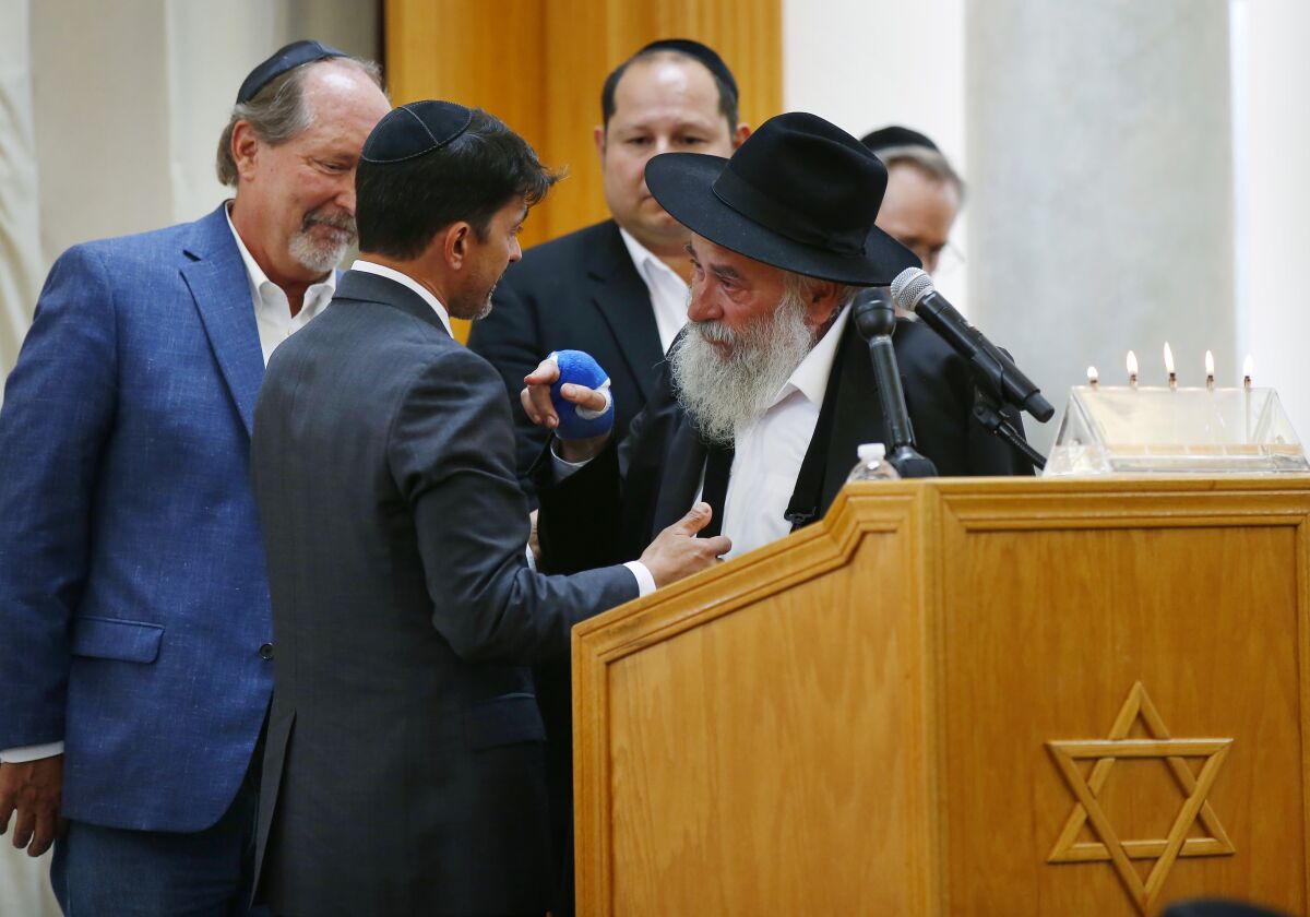Oscar Stewart, middle, is hugged by Rabbi Yisroel Goldstein, right, as Poway Mayor Steve Vaus, left, looks on.