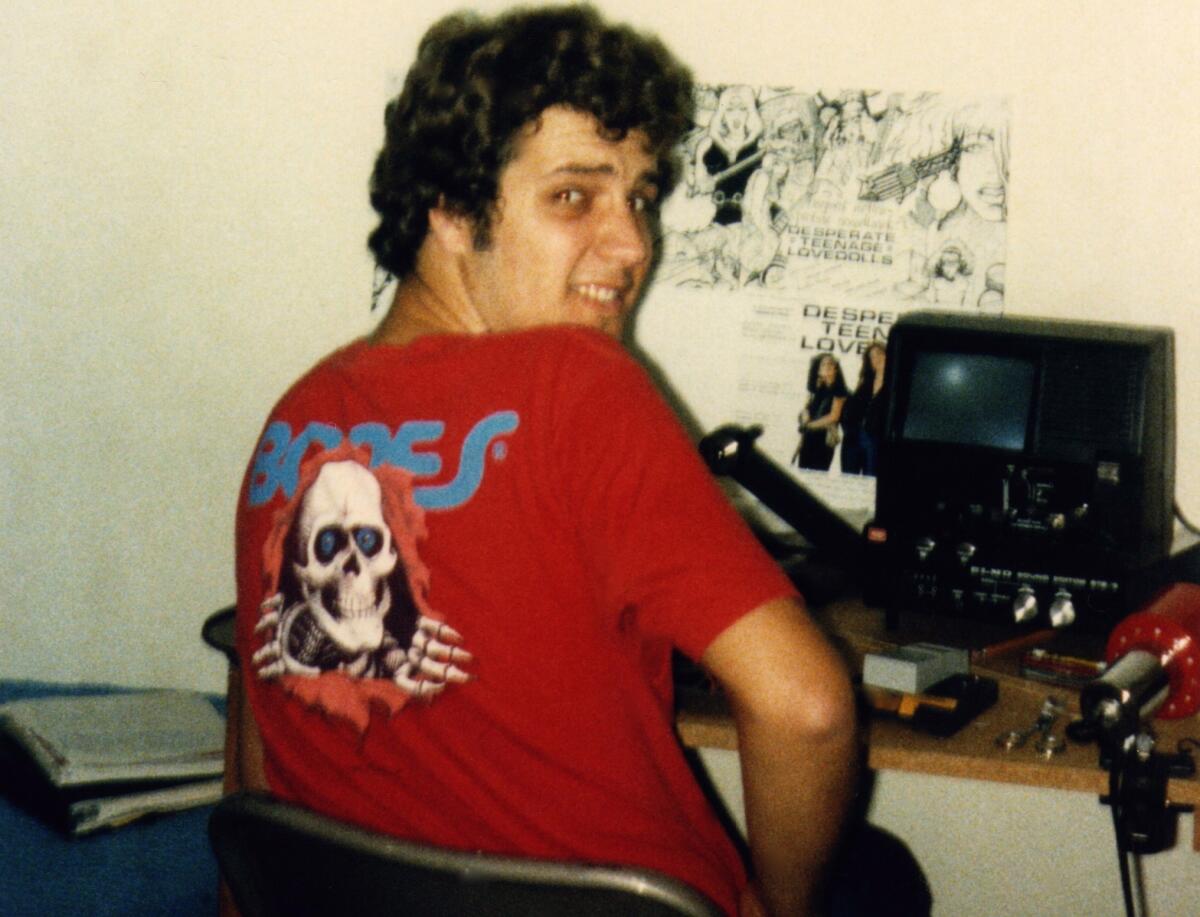 A man in a red T-shirt looks away from a desk and over his shoulder