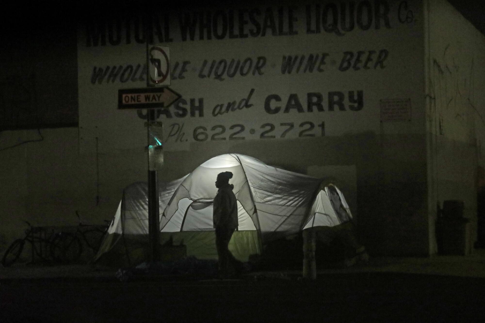A man walks past an illuminated tent used by a homeless couple on a sidewalk.