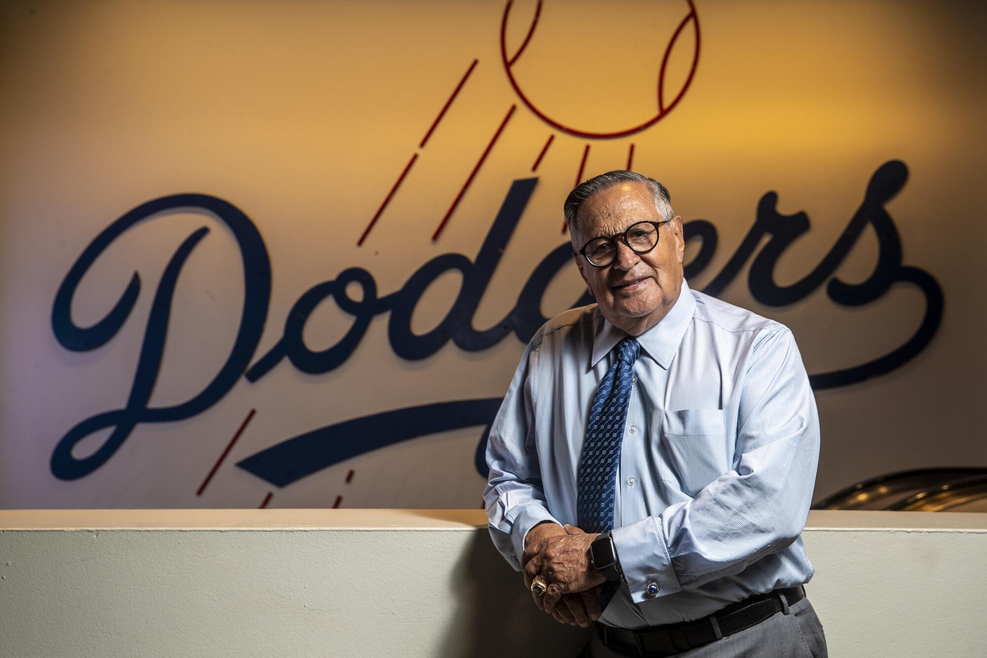 Veteran Dodgers broadcaster Jaime Jarrín stands in front of the Dodgers logo at Dodger Stadium.