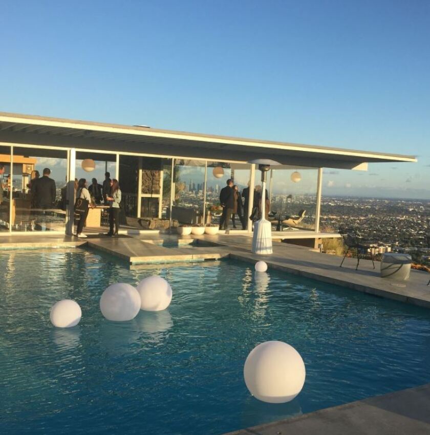 A glass house on a hillside overlooking a pool. 