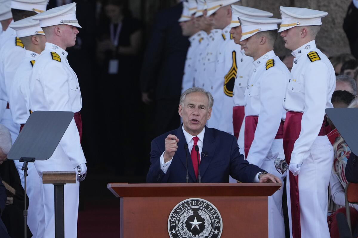 A man with gray hair, in a dark suit and red tie, gestures as he speaks at a lectern bearing a state of Texas seal 