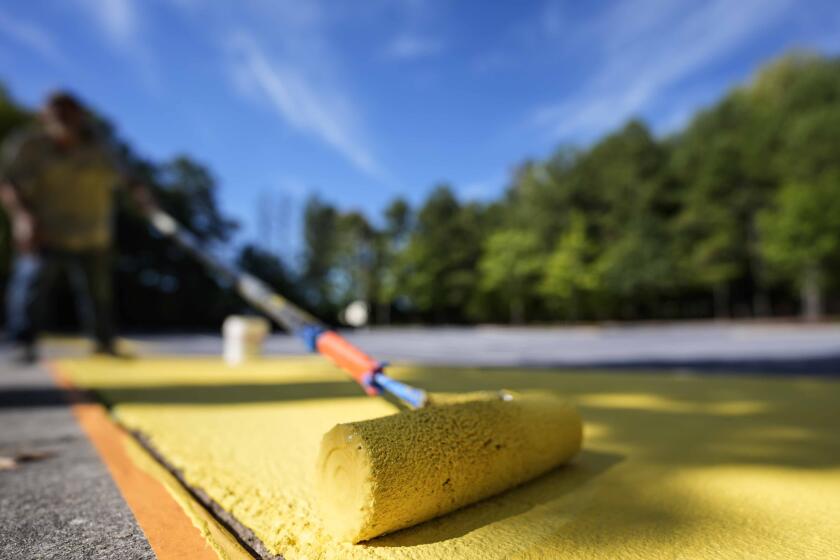 Ronnie Jefferies coloca pintura reflejante del calor en el estacionamiento de la Facultad de Ciencias, Artes y Emprendimiento para mantenerlo más fresco, el miércoles 4 de septiembre de 2024, en Mableton, Georgia. (AP Foto/Mike Stewart)