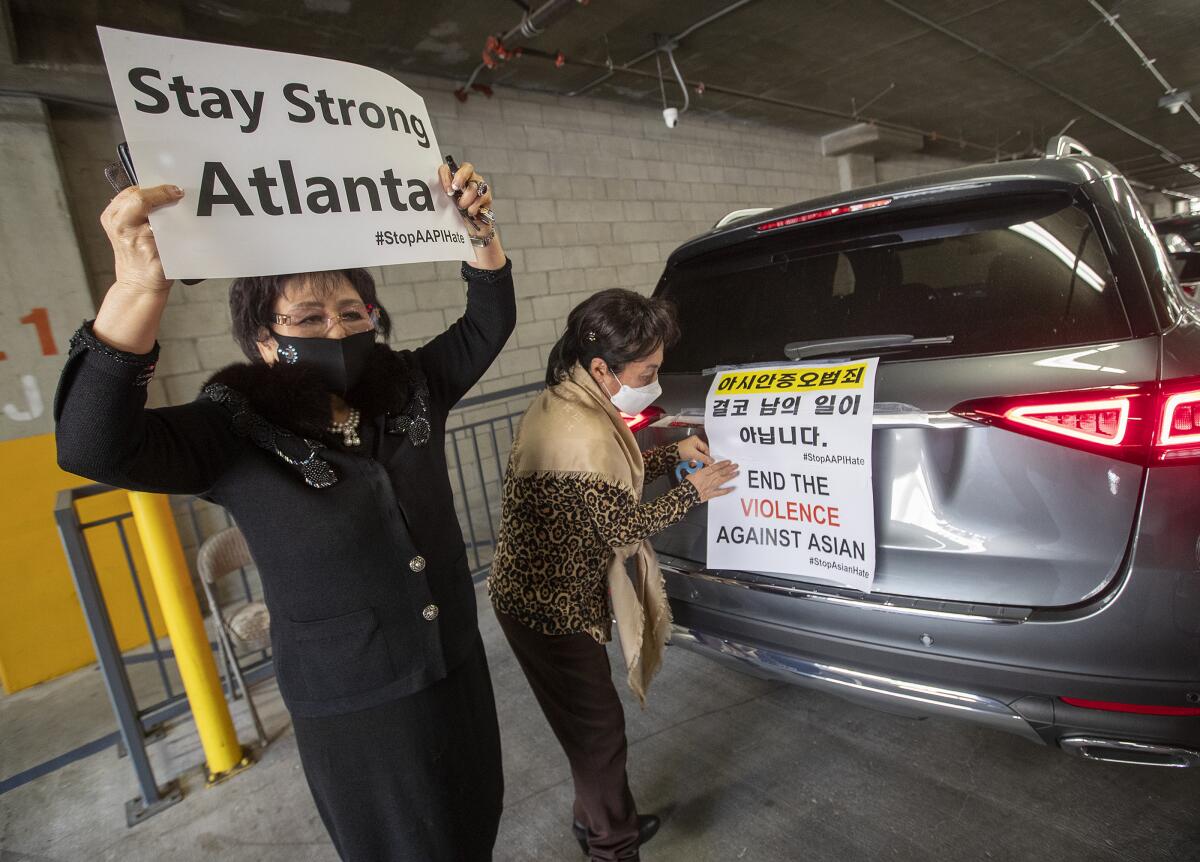 Two women with signs that say Stay Strong Atlanta and End the Violence against Asians behind a car in a parking garage