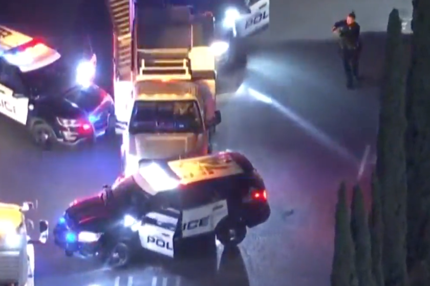 A police officer stands with gun drawn as two police vehicles block a utility truck.