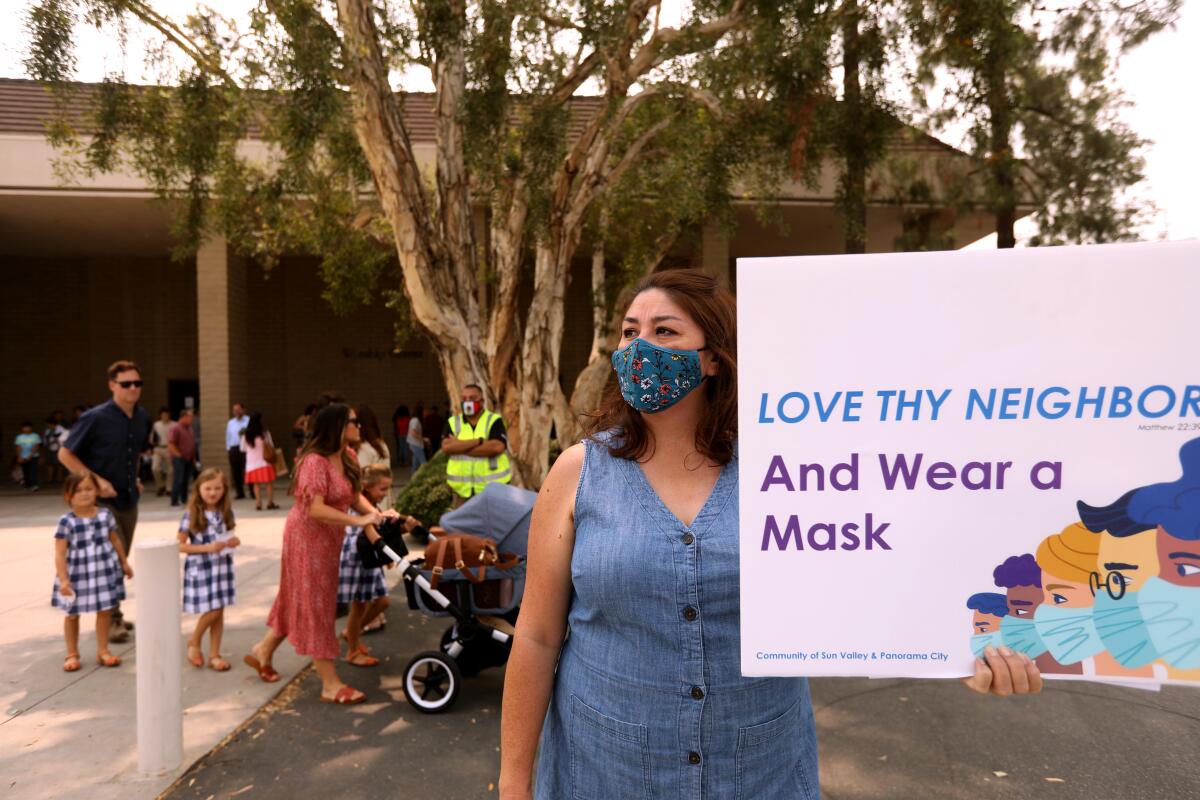 A woman holds a sign that says Love thy neighbor and wear a mask