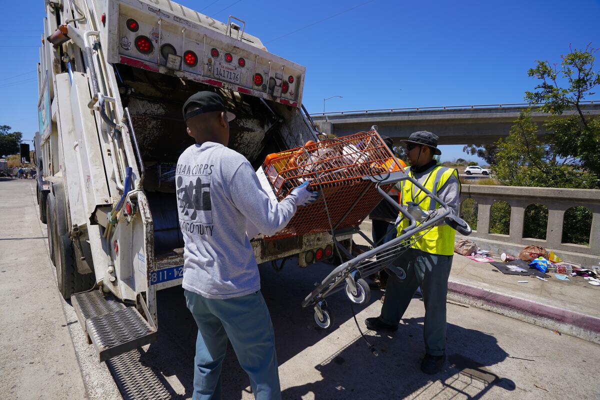 San Diego city workers throw a shopping cart into a trash truck after it was found in a homeless encampment on Anna Avenue.