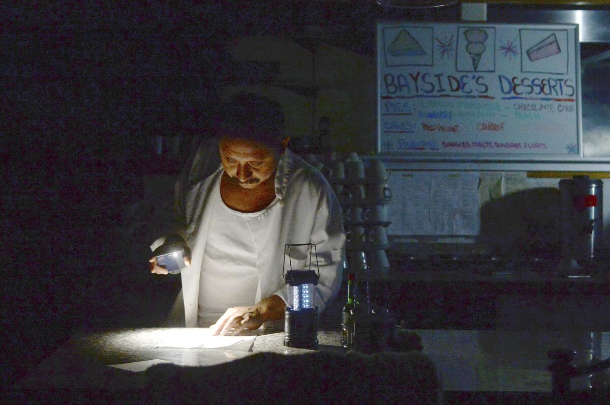 Carlos Lama of Bayside Cafe uses an LED lamp and light from his phone during a power outage