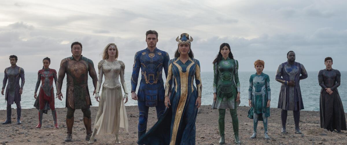 A line of superheroes standing on the beach in the movie "Eternals."