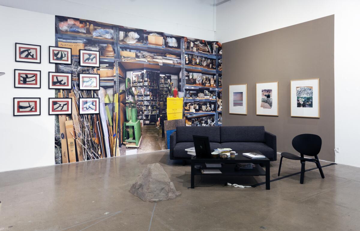 A black couch and a rock sit before a wall-sized vinyl that reveals the contents of an artist's studio. 