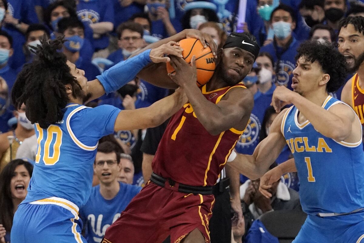 USC forward Chevez Goodwin and UCLA guard Tyger Campbell grapple for the ball as guard Jules Bernard watches.