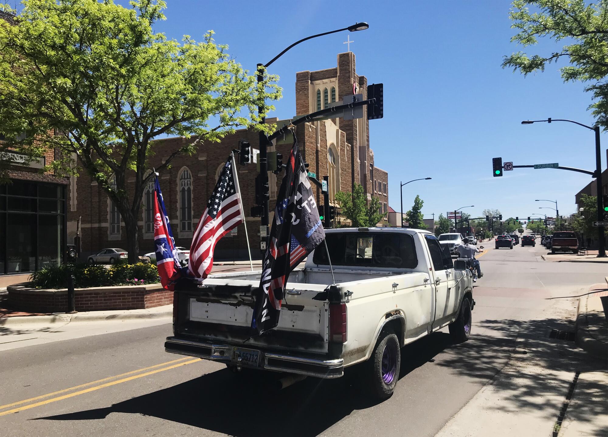 A truck drives through a downtown street with flags on the back