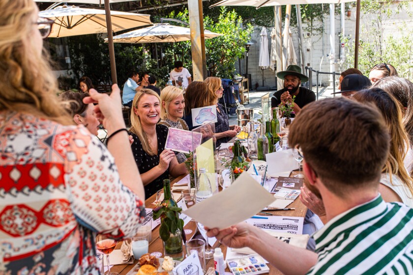 People on a long table hold up watercolor paintings