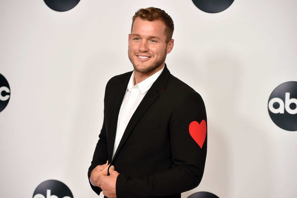 A man posing in black suit with a red heart on the sleeve.