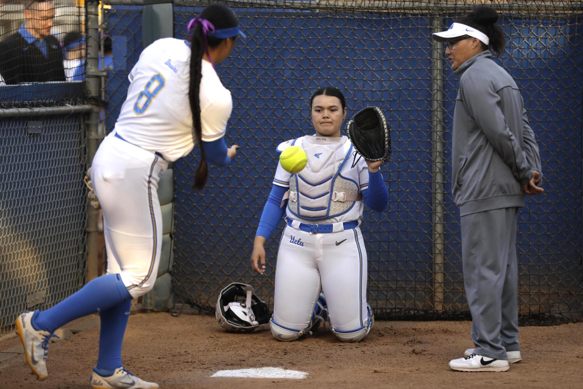 UCLA pitcher Megan Faraimo warms up with catcher Taylor Sullivan as pitching coach Lisa Fernandez observes in the bullpen