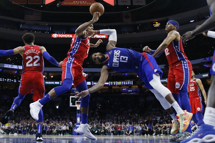 Clippers forward Paul George (13) tumbles to the court after attempting a layup between 76ers center Al Horford, left, and Tobias Harris (12) during a game Feb. 11, 2020, in Philadelphia.