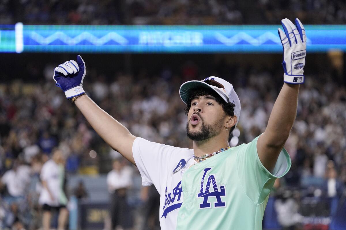 A man in a Dodgers uniform and hat cheers and raises his arms in the air in front of a crowd.