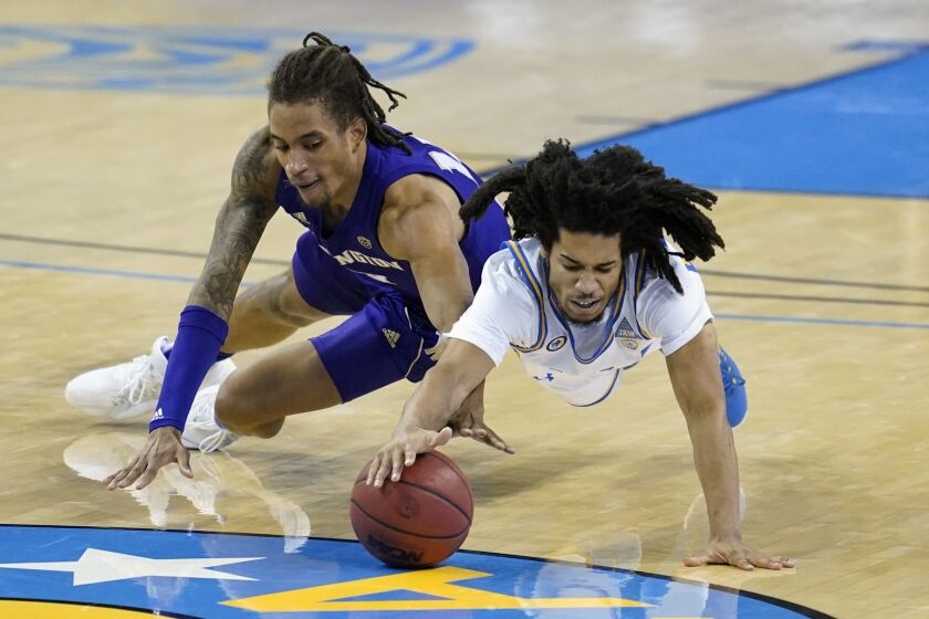 Washington forward Hameir Wright, left, and UCLA guard Tyger Campbell dive for a loose ball during the second half of an NCAA college basketball game Saturday, Jan. 16, 2021, in Los Angeles. (AP Photo/Ashley Landis)