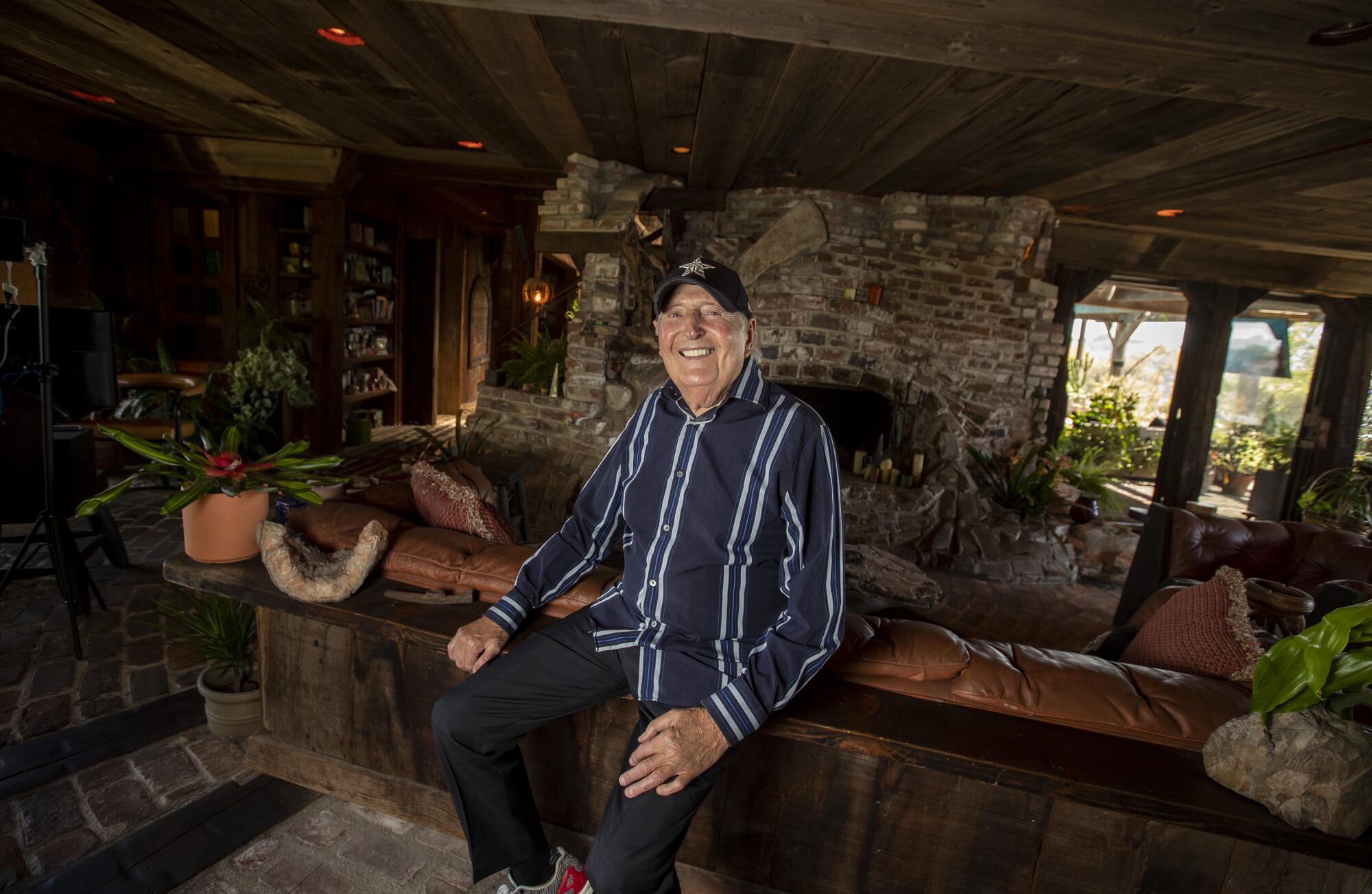 Sid Krofft sits in a room made of stone and wood