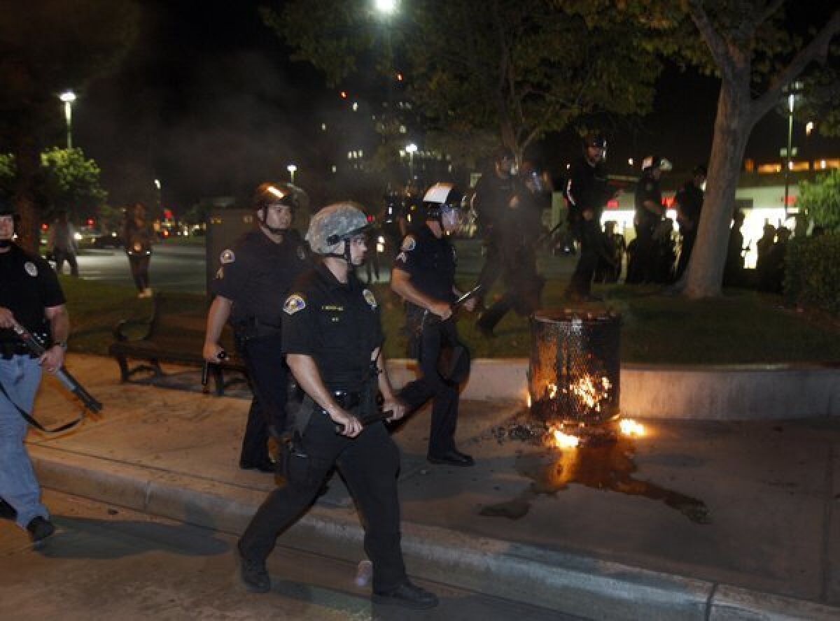 Anaheim police dressed in riot gear pass by burning trash during violent protests last summer.