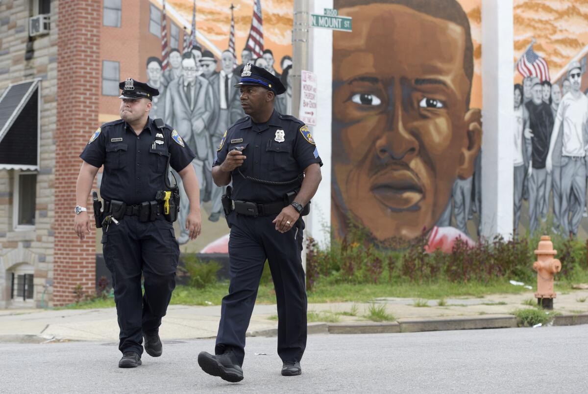 Baltimore police walk near a mural depicting Freddie Gray after prosecutors dropped remaining charges against the three Baltimore police officers who were still awaiting trial in Gray's death.