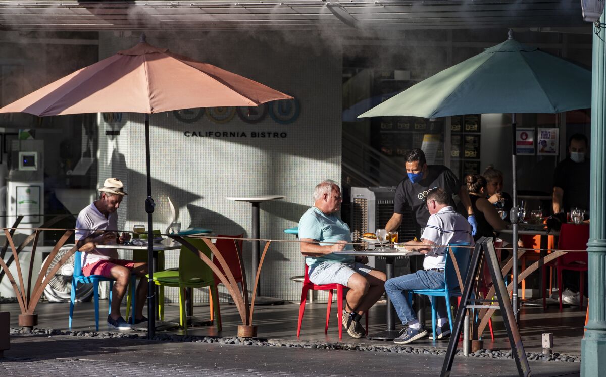 A waiter wearing a mask serves diners outside at Lulu's California Bistro in Palm Springs in July.