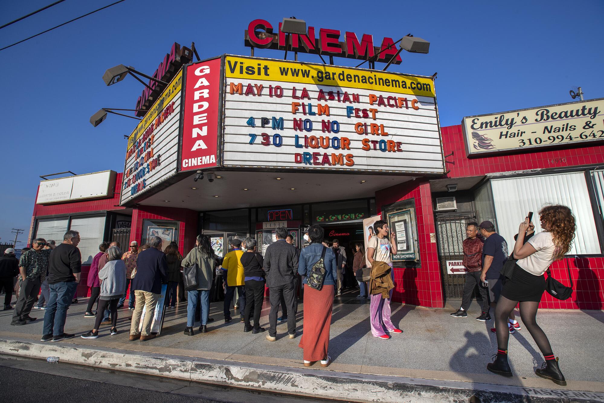 People stand on the sidewalk outside a small movie theater with an old-fashioned marquee