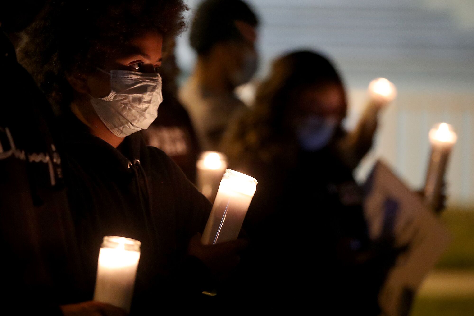 People in masks hold candles at a vigil