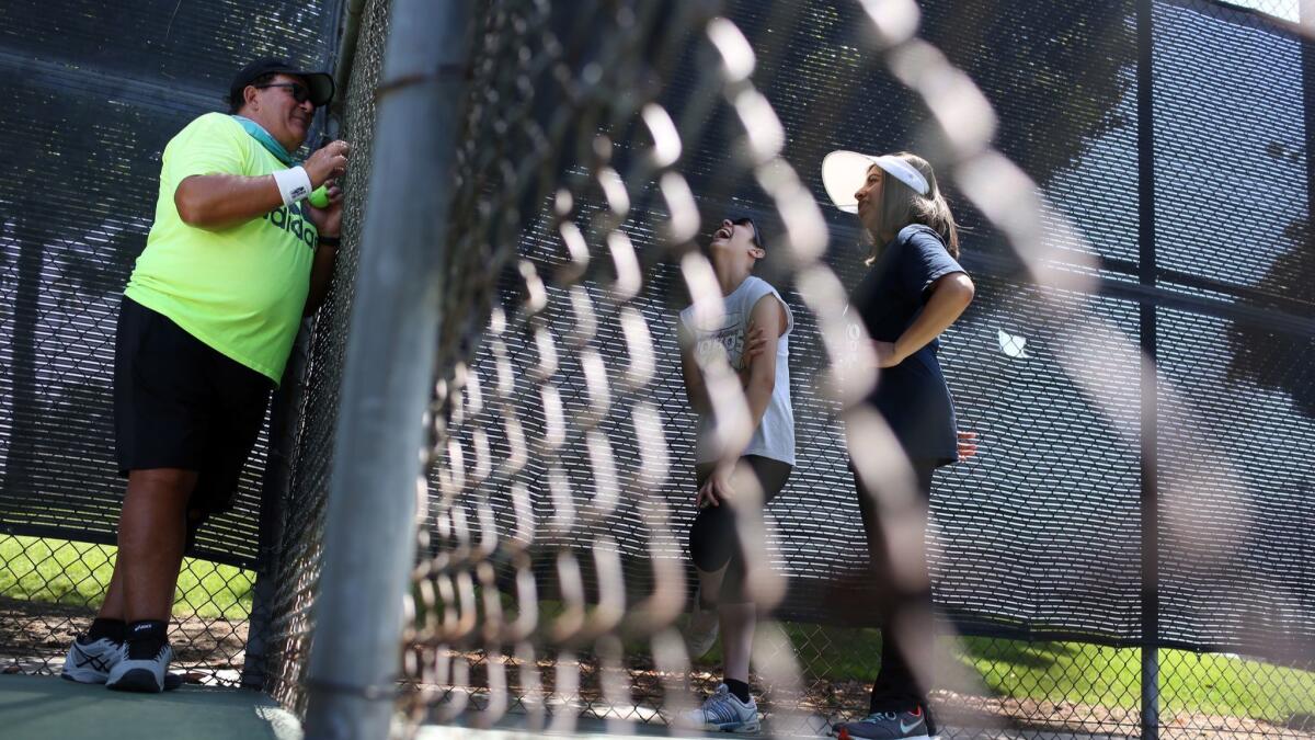 Joe Serrano, left, offers tennis instruction to Nadia Larios, center, and Paola Rocha, right, in Downey. Serrano is part of a group of mostly retired men who play tennis about twice a week.