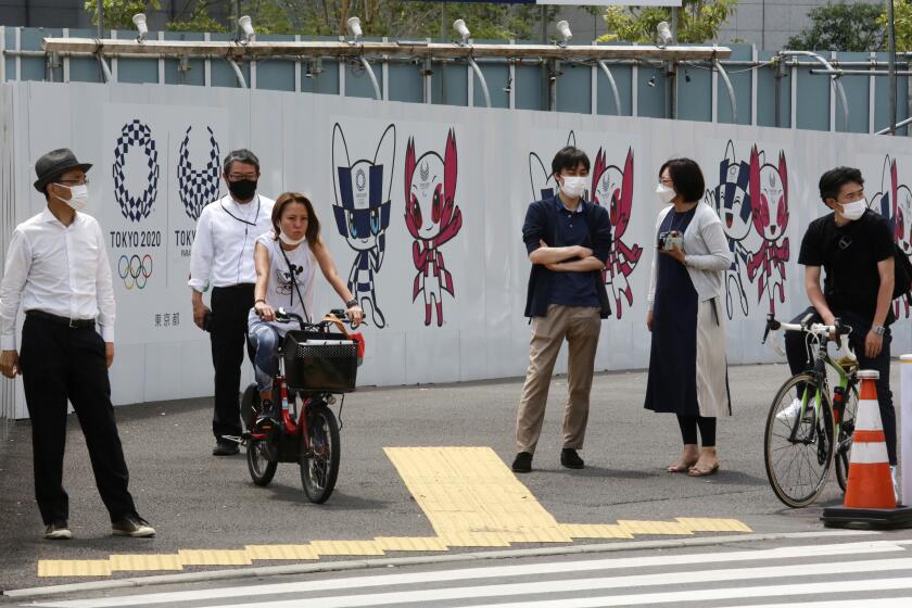 People stand by posters to promote the Tokyo Olympic Games scheduled to start in the summer of 2021, in Tokyo, Monday, May 24, 2021. (AP Photo/Koji Sasahara)