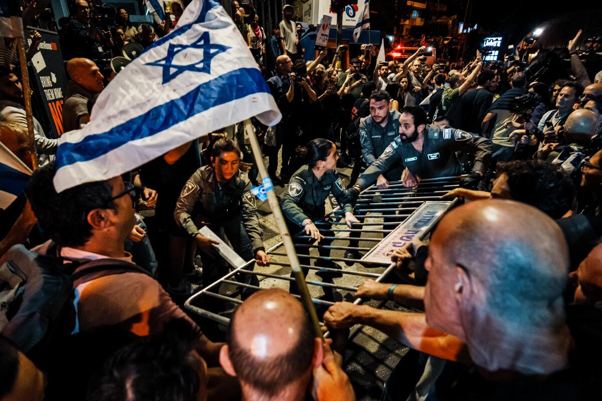A blue-and-white flag is hoisted as people tussle over a metal barricade in a crowd