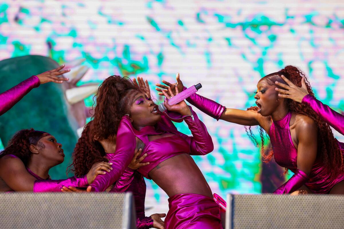 A female rapper in purple outfit performs onstage with dancers.