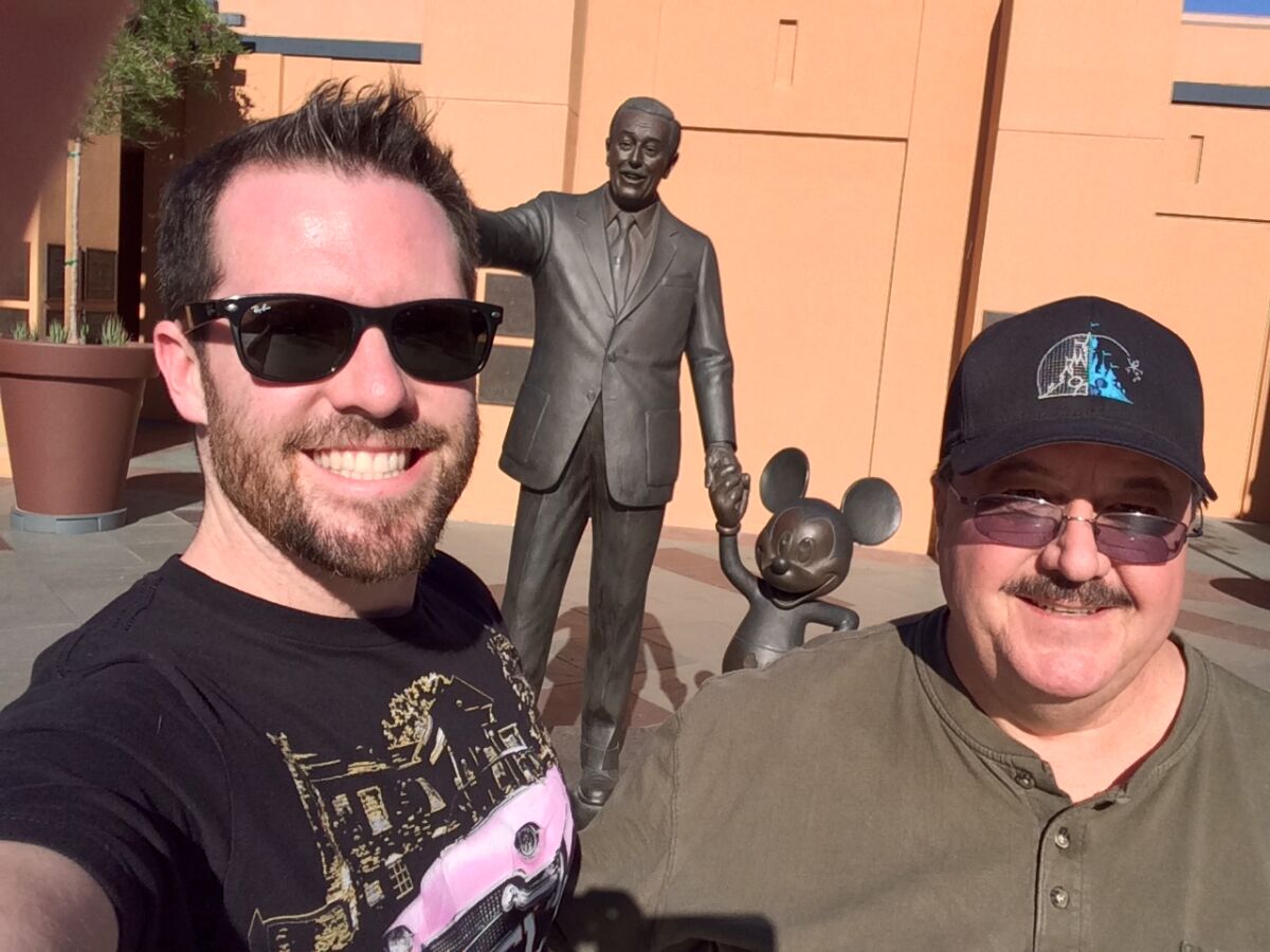 A father and son picture in front of a statue of Walt Disney and Mickey Mouse. 