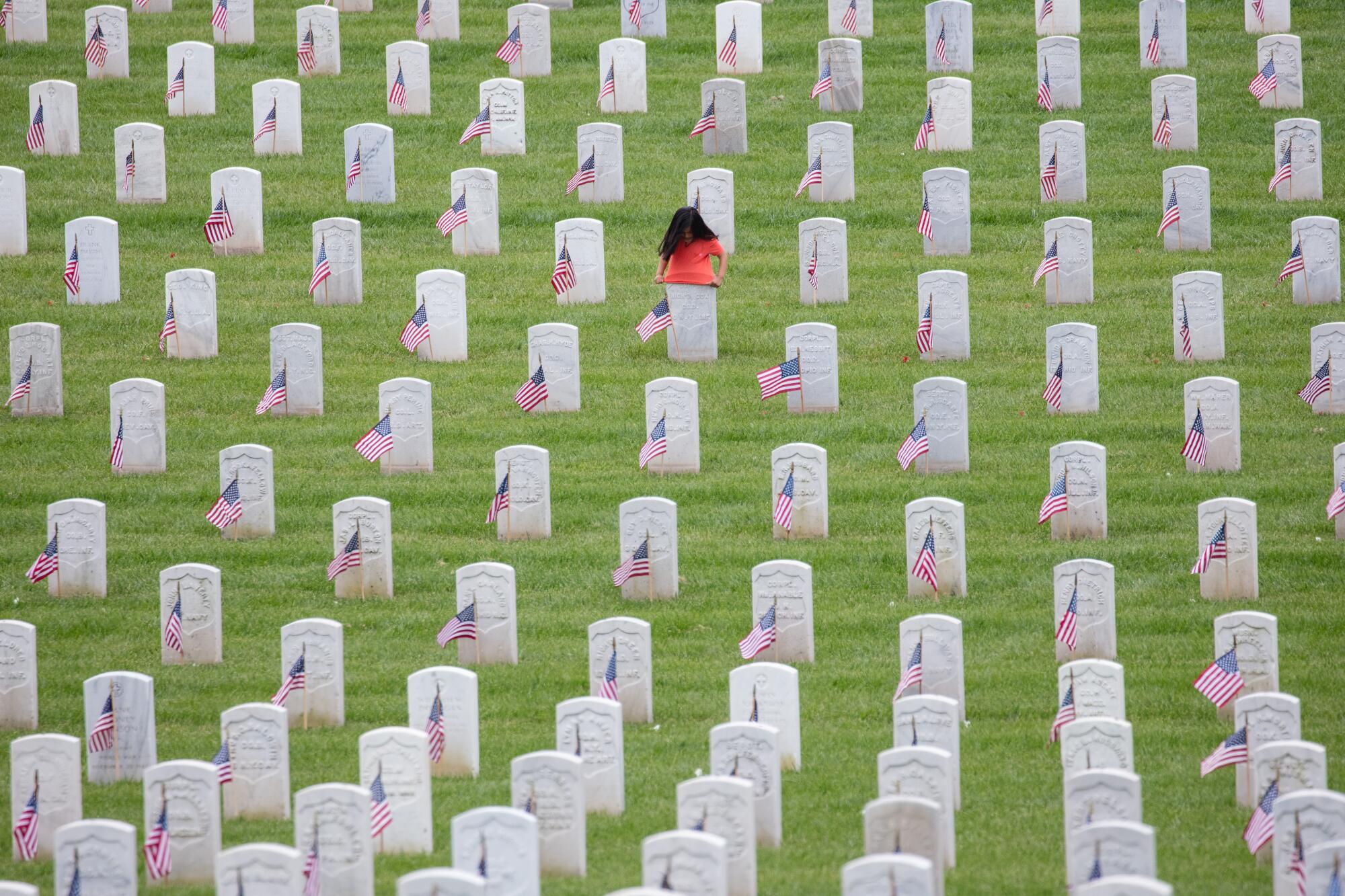 A young girl tries to fit her shirt over the top of a headstone on Memorial Day, at the Los Angeles National Cemetery