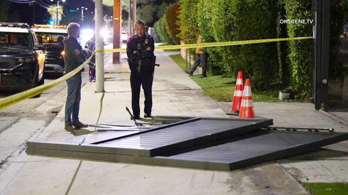 A gate lies on the ground while a police officer and another person stand nearby at night.