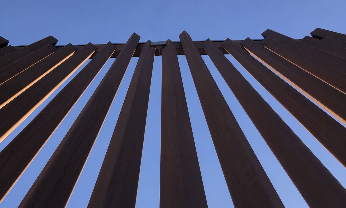 Metal bars of a border barrier stretch up toward a clear blue sky