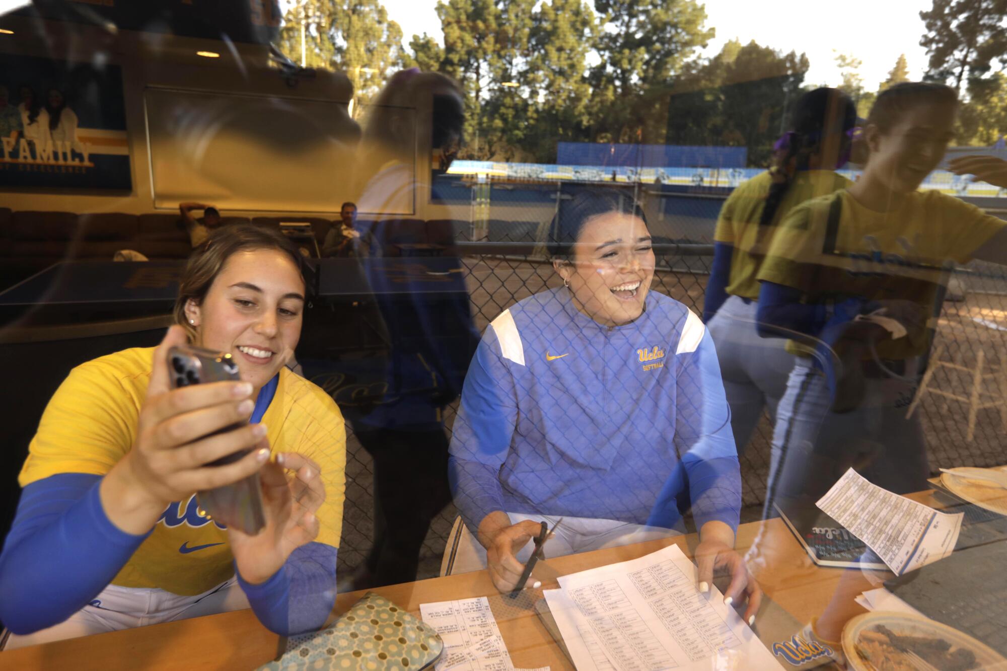 UCLA bullpen catchers Sara Rusconi Vicinanza, left, and Taylor Sullivan laugh while looking at scouting reports
