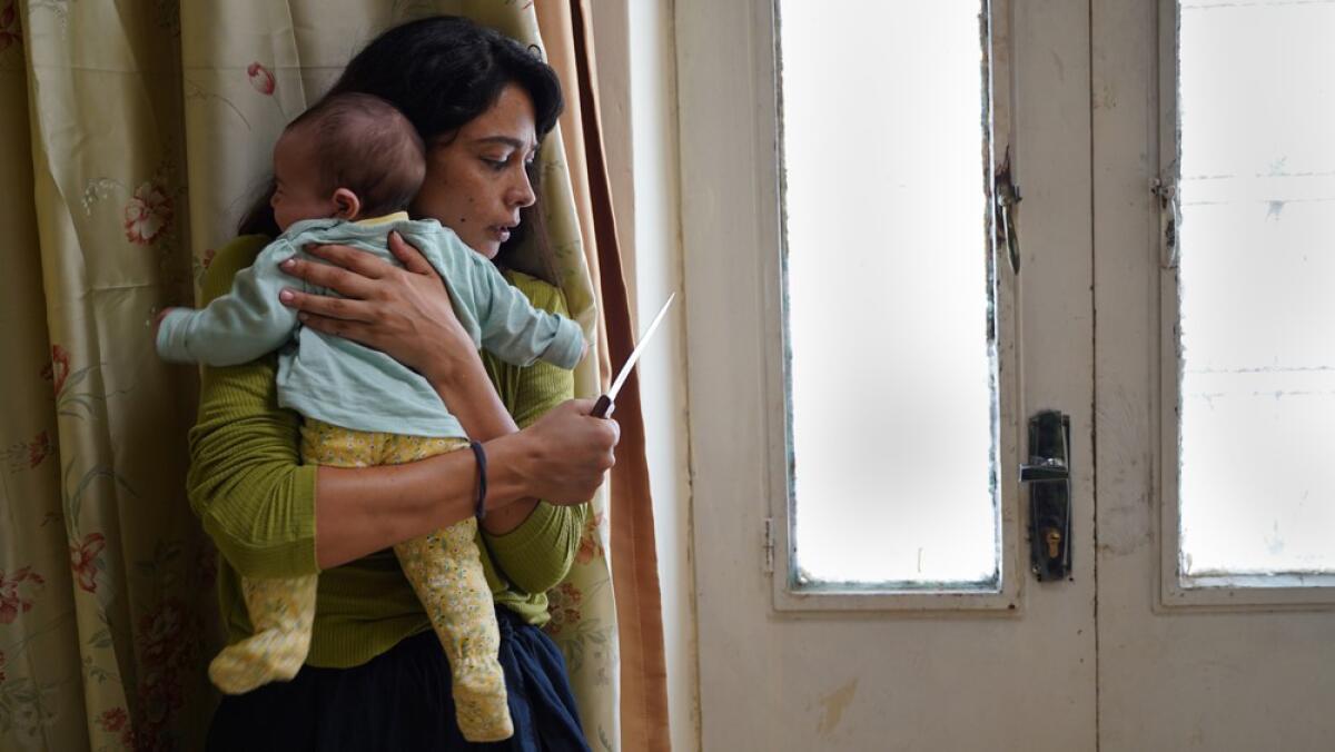 A woman holds a knife in one hand as she clutches a baby to her chest.