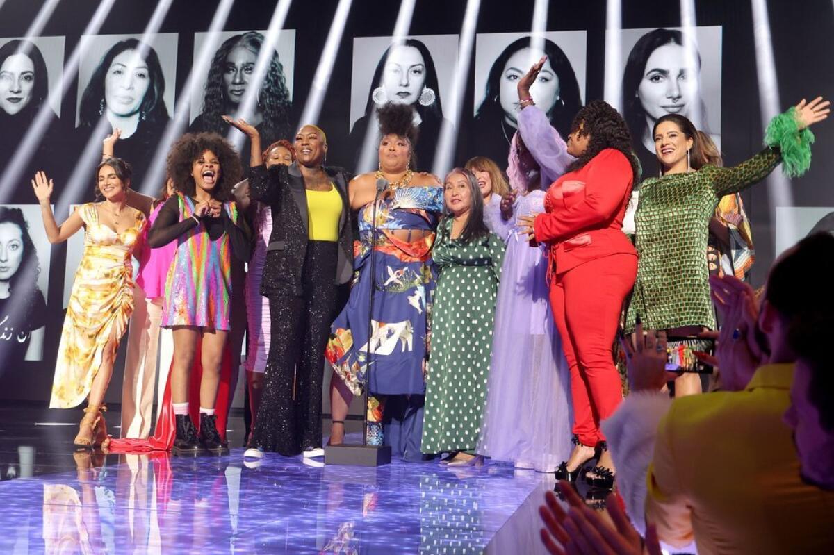 Lizzo standing onstage surrounded by activists accepting an award at the People's Choice Awards 2022