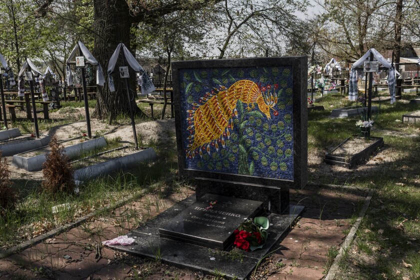 A view of a cemetery shows one tomb festooned with a bright painting of a fantastical flying creature in orange and red.